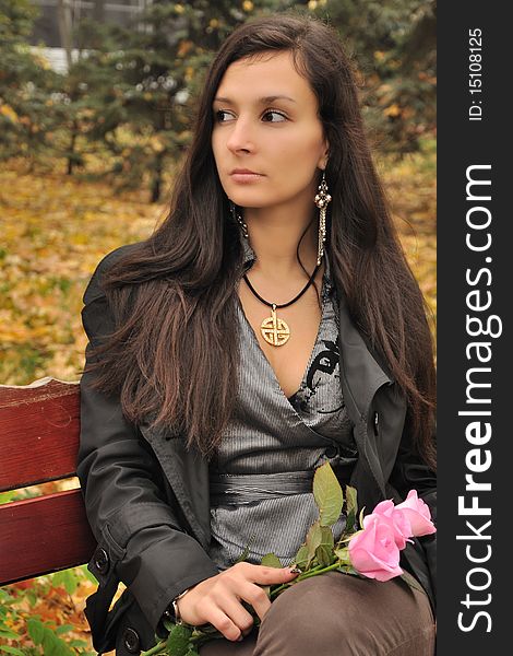 Sexual young girl with roses sits at the autumn city park