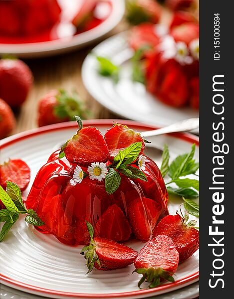 Strawberry jelly with the addition of halfs of fresh strawberries and mint leaves on a white plate.