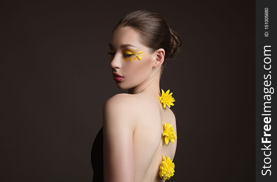 Young woman spa. Yellow flowers along her back, face and body in the shade. Back view. Dark background