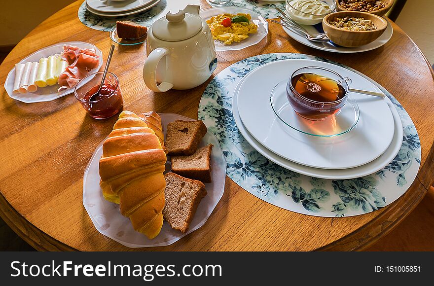 Breakfast table with variety of foods including cereals, cheese, yogurt, scrambled eggs, fruit, croissant and drinks such as tea, coffee and orange juice. Breakfast table with variety of foods including cereals, cheese, yogurt, scrambled eggs, fruit, croissant and drinks such as tea, coffee and orange juice.