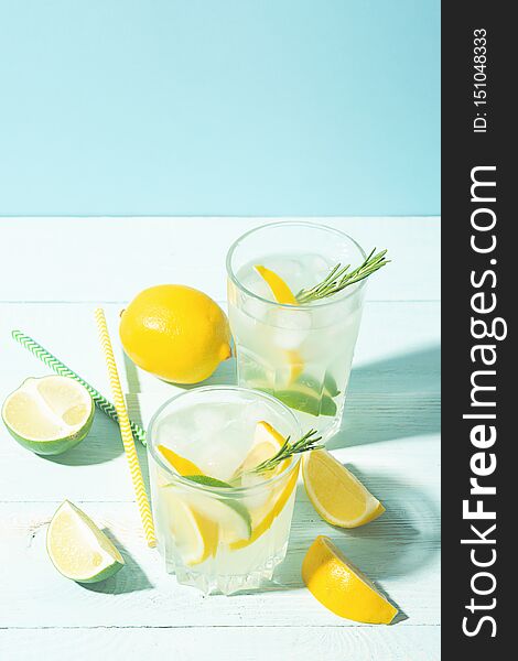 A drink of lemon and lime in an elegant glass on a blue background with bright sunshine. Summer cocktail or mojito. Vertical frame. Copy space. Selective focus.
