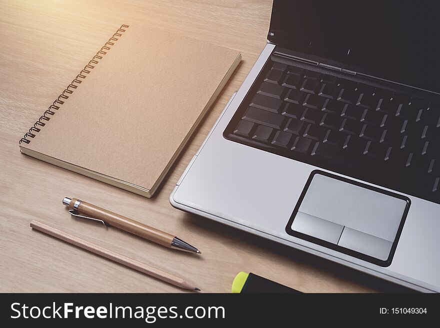 Workspace with diary or notebook and laptop, pen, pencil, hightlight pen, metal clip on wooden background