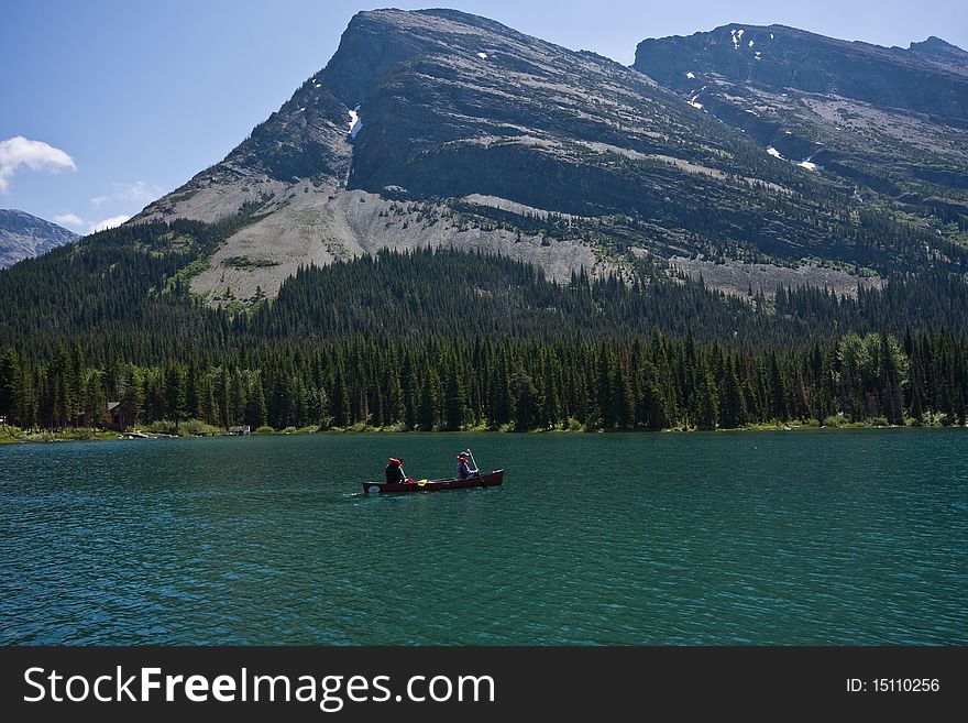 Two people in lifejackets go canoeing on the lake surrounded by mountains. Two people in lifejackets go canoeing on the lake surrounded by mountains