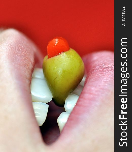 A green olive held in girls teeth beneath wet lips. A green olive held in girls teeth beneath wet lips