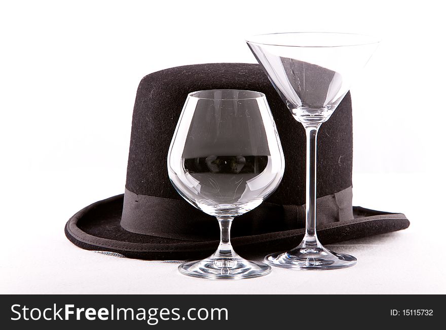 Two empty wine martini or cognac glasses standing empty next to a top hat on a white background. Two empty wine martini or cognac glasses standing empty next to a top hat on a white background