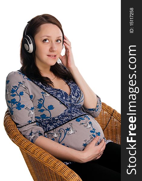 Beautiful pregnant woman sits in a wicker chair and listens to music, isolated on white. Beautiful pregnant woman sits in a wicker chair and listens to music, isolated on white