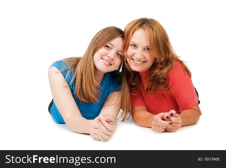 Two beautiful smiling girls lie on a floor, isolated on white