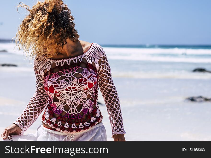 Beautiful woman with hand made dress enjoy the beach in summer vacation - outdoor leisre activity in tropical place - blue ocean and sky in background - curly hair moved by the wind