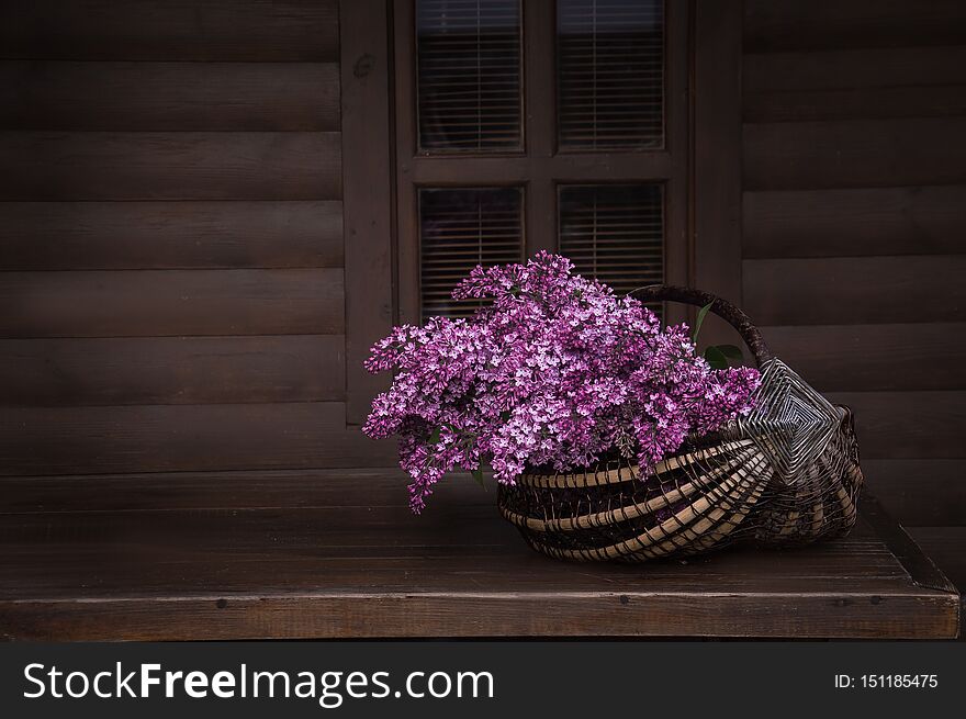 Bouquet of aroma lilacs in a basket on a dark wooden background