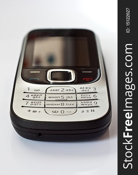 Mobile telephone with black and silver body lies on a white surface