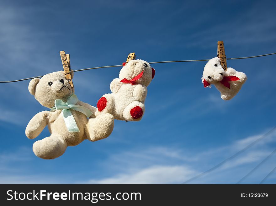 Three teddies hung out to dry on a clothesline, with blue skies in the background