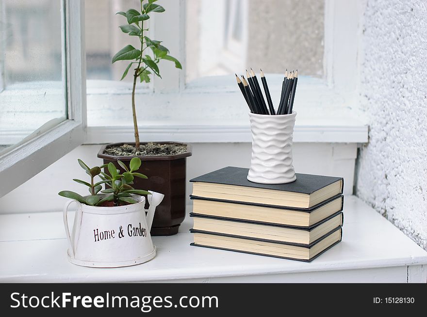 A stack of books, flowers and pencils in a cozy white verandah