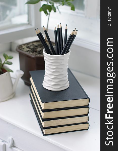 A stack of books, flowers and pencils in a cozy white verandah