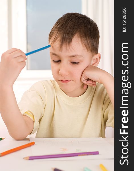 Boy with a pencil sitting at the table and draws. Boy with a pencil sitting at the table and draws