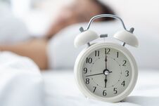 Alarm Clock On White Bad With Light From Window, Selective Focus Stock Photo