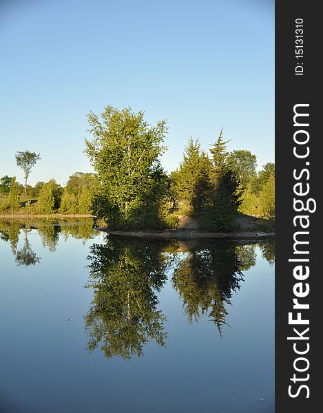 The calm waters of the pond reflect the skyline above almost as well as a mirror. The calm waters of the pond reflect the skyline above almost as well as a mirror.