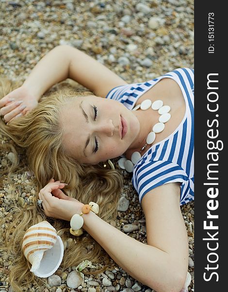 The beautiful girl in a stripped vest lies on sea coast with cockleshells