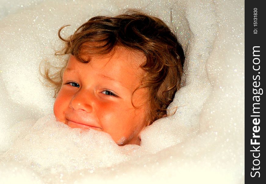 A toddler boy in a bathtub that has his body covered by bubbles and only his face showing with all the bubbles around it. A toddler boy in a bathtub that has his body covered by bubbles and only his face showing with all the bubbles around it.