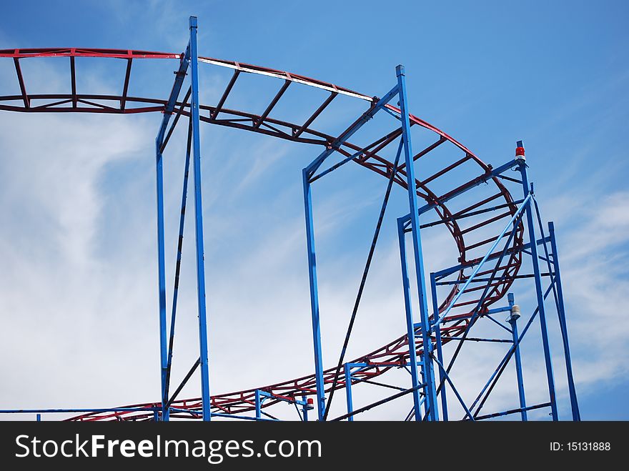 The curve of older metal roller coaster tracks that are red and blue taken at the Sylvan Beach New York amusement park on Lake Oneida with a cloudy blue sky as the background.