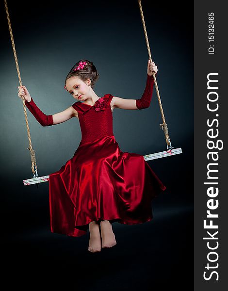 Young model in red dress on swing on black background. Young model in red dress on swing on black background