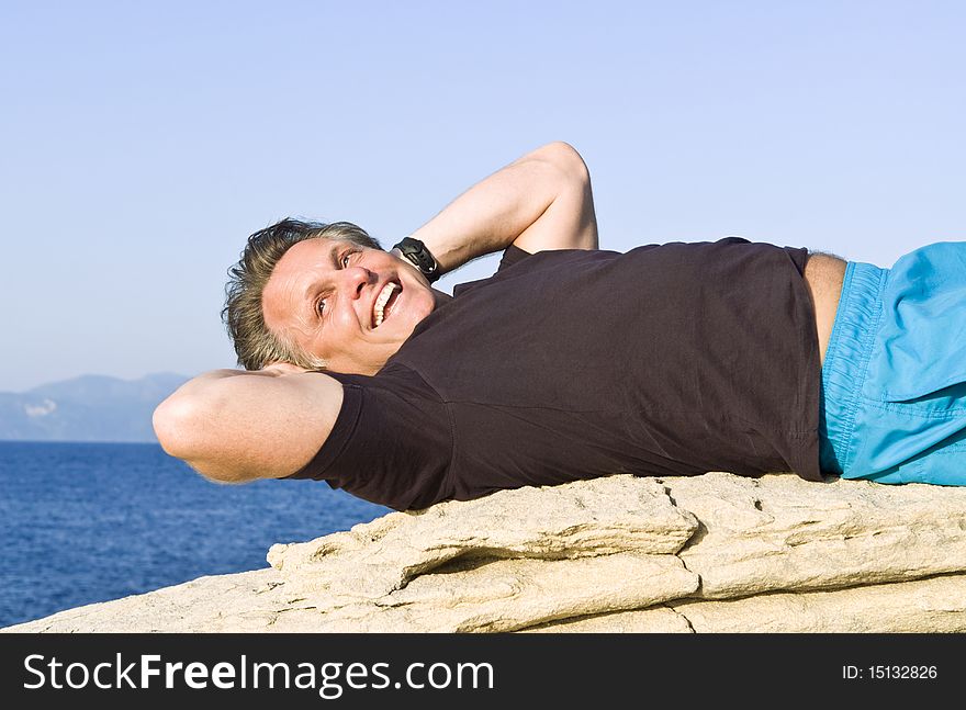 A color portrait photo of a smiling man in his forties laying on a rock and relaxing during his vacation. A color portrait photo of a smiling man in his forties laying on a rock and relaxing during his vacation.