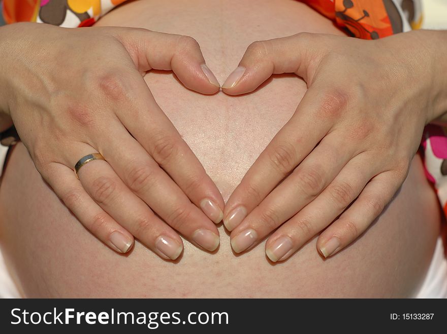 Pregnant woman with hands in the shape heart on the belly
