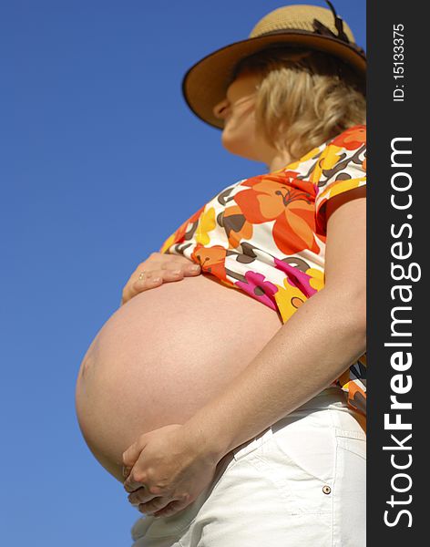 Pregnant woman with hands on the belly relating to the blue sky