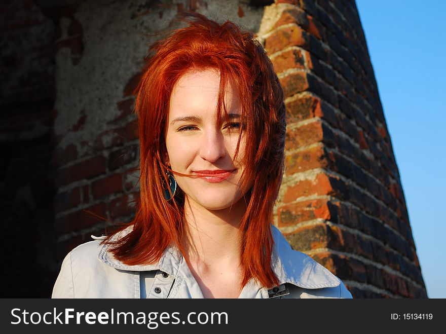 Portrait of a young woman with red hair, standing near old building in a sunny windy day. Portrait of a young woman with red hair, standing near old building in a sunny windy day.