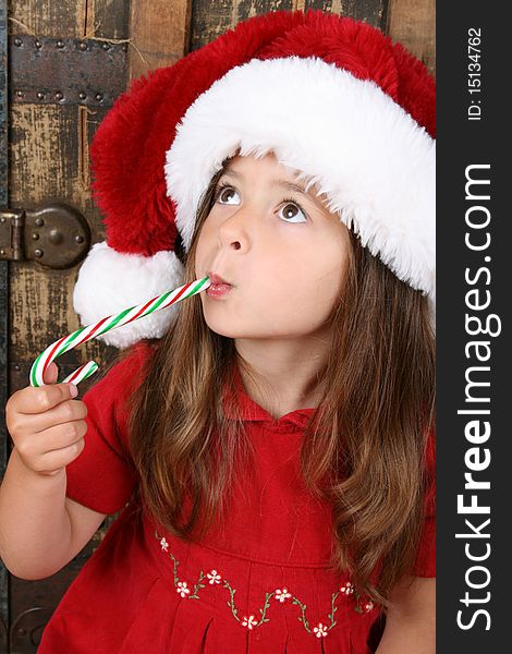 Cute brunette girl wearing a christmas hat, eating candy. Cute brunette girl wearing a christmas hat, eating candy