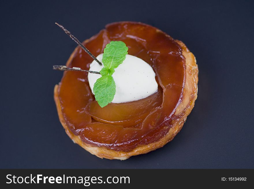 Individual apple tart Tatin with a scoop of a Chantilly cream, mint and caramelised (edible)vanilla pod. Shot from above, isolated on black.Classic french dessert