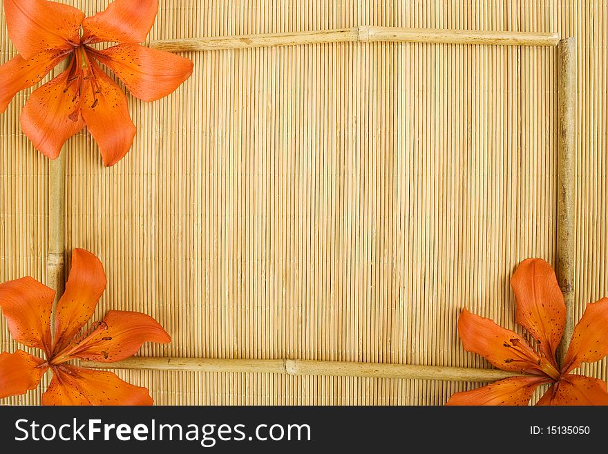 On a wooden surface of the orange flowers tiger lilies and bamboo sticks arranged in a frame. On a wooden surface of the orange flowers tiger lilies and bamboo sticks arranged in a frame