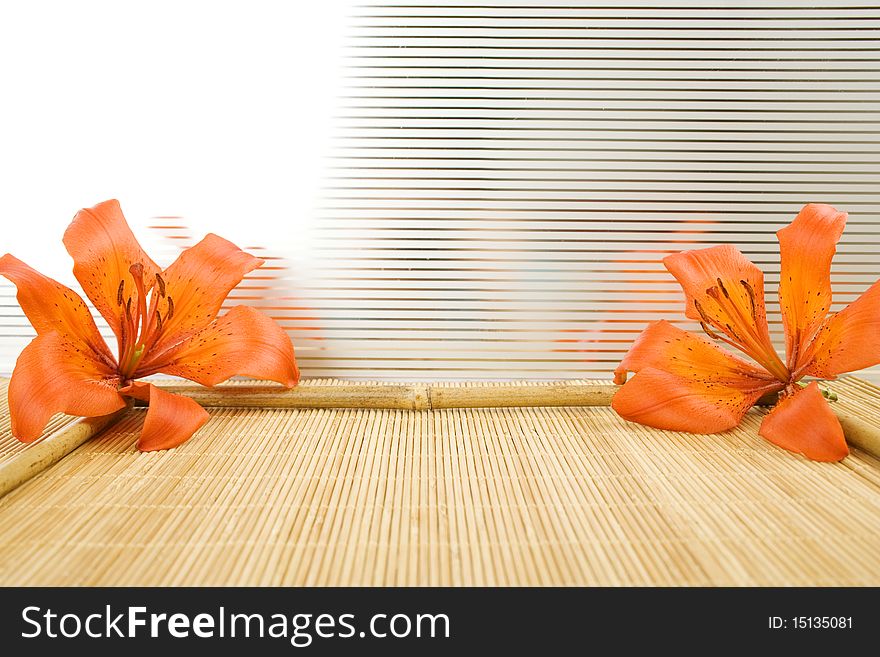 On a wooden surface of the orange flowers tiger lilies and bamboo sticks arranged in a frame. On a wooden surface of the orange flowers tiger lilies and bamboo sticks arranged in a frame