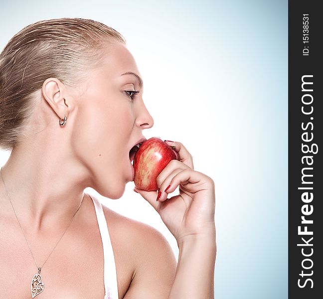 Portrait of young beautiful woman biting apple on blue back