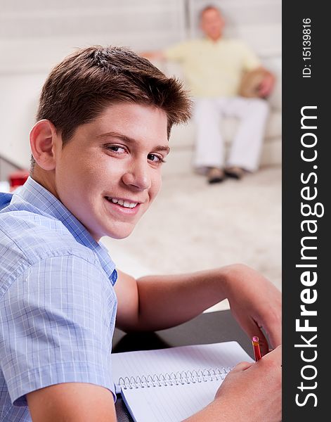 Close-up of young boy studying and looking at camera as father relaxes on the couch in the background. Close-up of young boy studying and looking at camera as father relaxes on the couch in the background