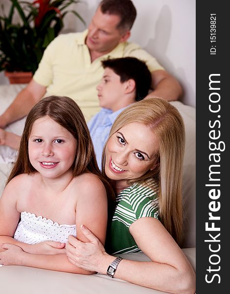 Mom and daughter in focus facing camera with father and boy in the background, all relaxing on couch. Mom and daughter in focus facing camera with father and boy in the background, all relaxing on couch