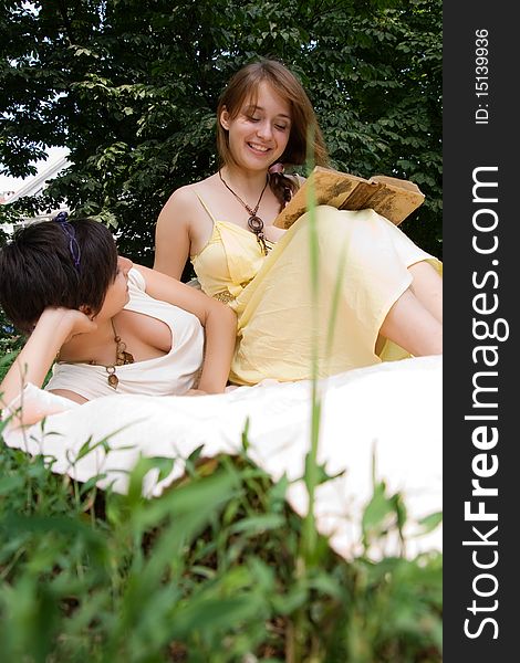 Two young chicks sitting on the coverlet upon green grass reading a book. Two young chicks sitting on the coverlet upon green grass reading a book