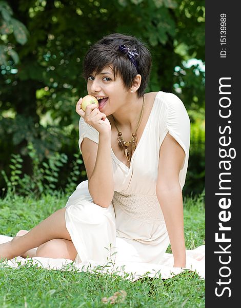 Healthy and beautiful young woman eats an appla sitting on coverlet upon green grass. Healthy and beautiful young woman eats an appla sitting on coverlet upon green grass