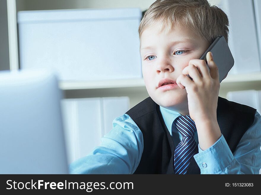 Young confident executive businessman boss boy in office talks on the phone sitting at the desk with laptop.