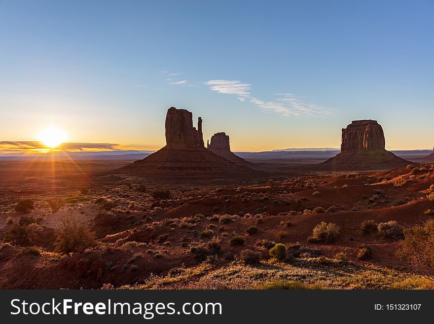 Monument Valley desert at sunrise. Navajo Tribal Park in the Arizona-Utah border USA. Sun rising behind the red rocks, clear sky background. Monument Valley desert at sunrise. Navajo Tribal Park in the Arizona-Utah border USA. Sun rising behind the red rocks, clear sky background
