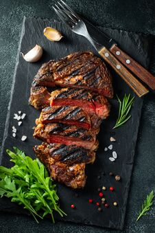 Sliced Steak Ribeye, Grilled With Pepper, Garlic, Salt And Thyme Served On A Slate Cutting Board On A Dark Stone Royalty Free Stock Photo