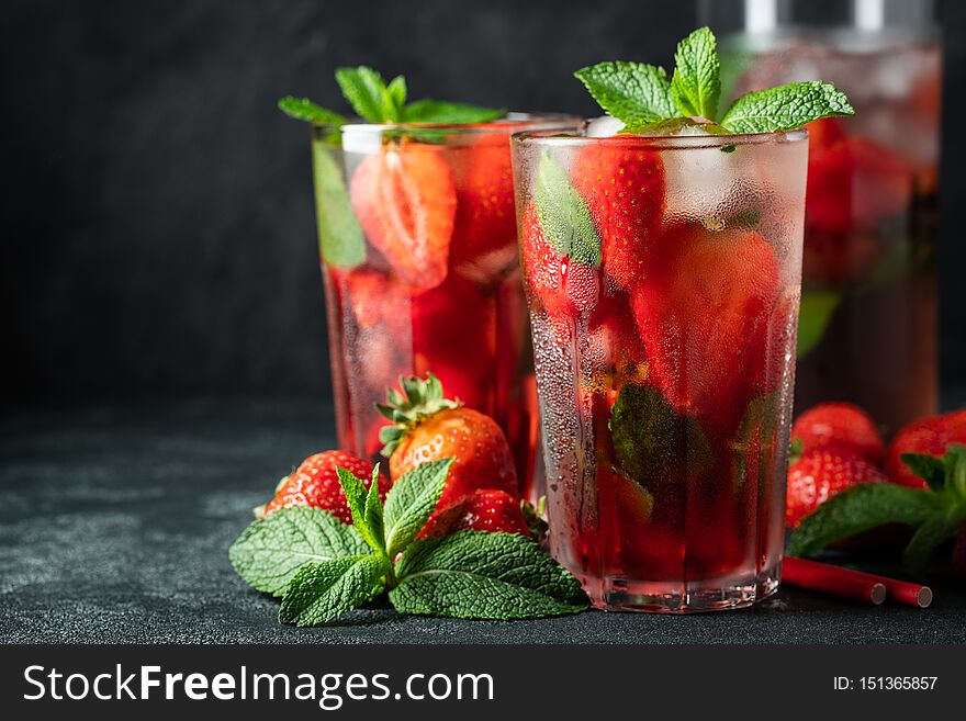 Fresh lemonade with ice, mint and strawberry on top in glass on black table background, copy space. Cold summer drink. Sparkling glasses with berry cocktail.