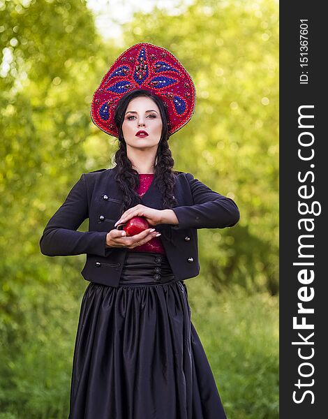 Fashion Brunete Woman In Russian Style Kokoshnik Outdoors Against Nature Background. Posing With Apple