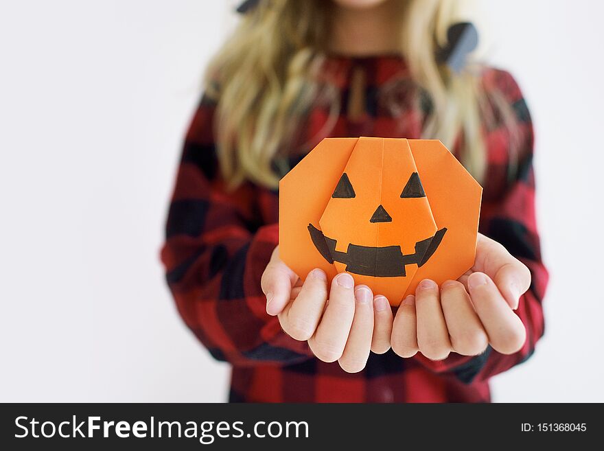 Paper pumpkin origami in the hands of a child on a white background