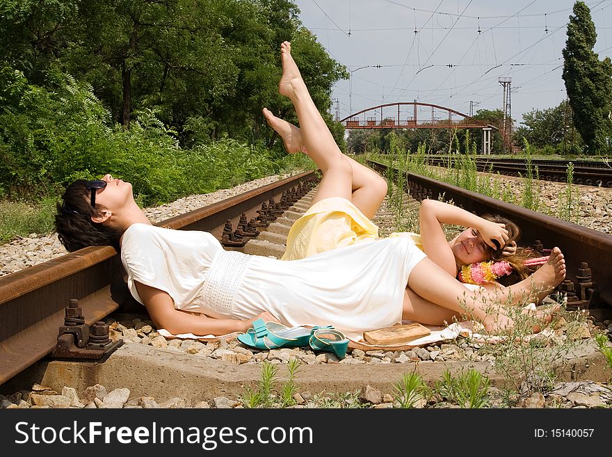 Young girls laying on the railroad in the middle of a bright day. Young girls laying on the railroad in the middle of a bright day