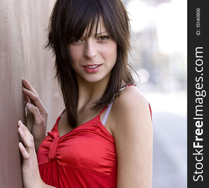 Very good looking girl leaning against a wall smiling and looking towards the camera. Very good looking girl leaning against a wall smiling and looking towards the camera