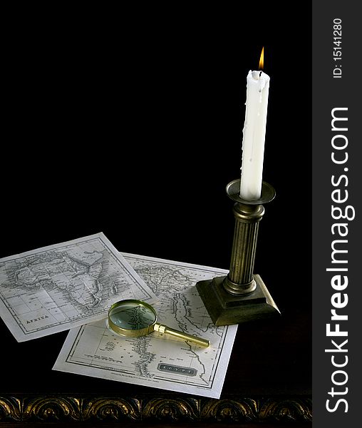 A candle with old maps and magnifying glass