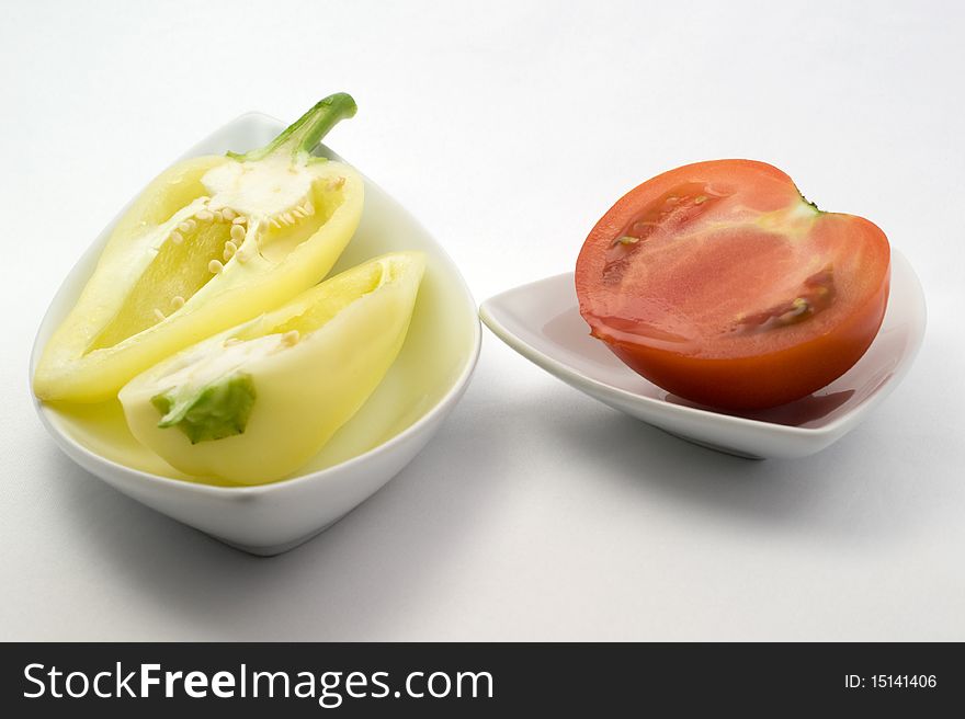 Fresh half tomato and sweet peppers on a plate on a white background. Fresh half tomato and sweet peppers on a plate on a white background