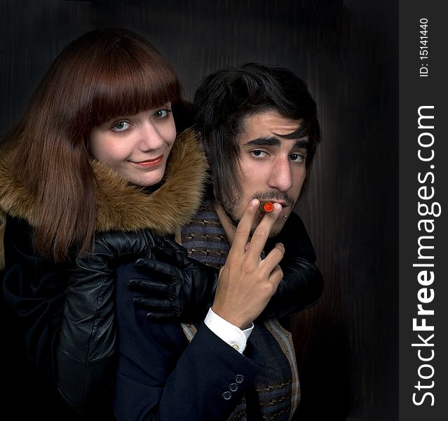 Portrait of young man and young women with cigar on dark background