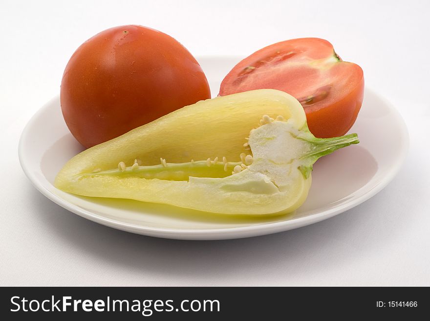 Fresh tomatoes and sweet peppers on a plate on a white background. Fresh tomatoes and sweet peppers on a plate on a white background