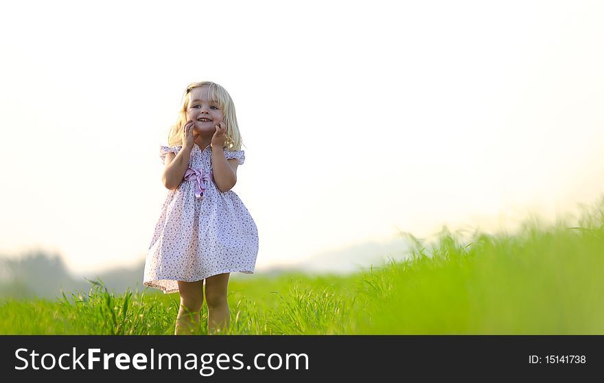 Adorable little girl stands in a meadow at sunset. Adorable little girl stands in a meadow at sunset